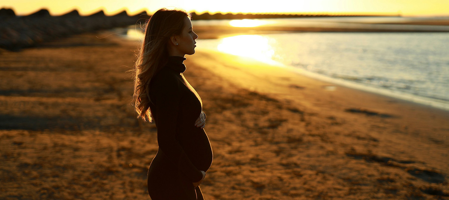 Pregnant woman standing on the beach.